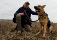man in a stubble field with a young German Shepherd