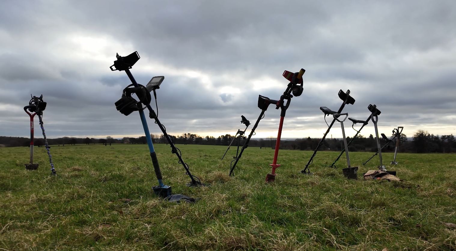 a group of metal detectors leaning on spades with a cloudy sky